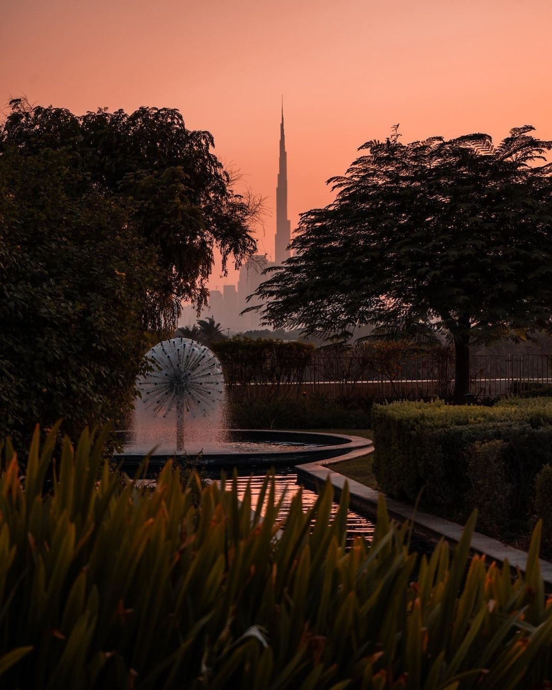 The Hanging Garden fountain at Raffles Dubai with Burj Khalifa silhouette at sunset